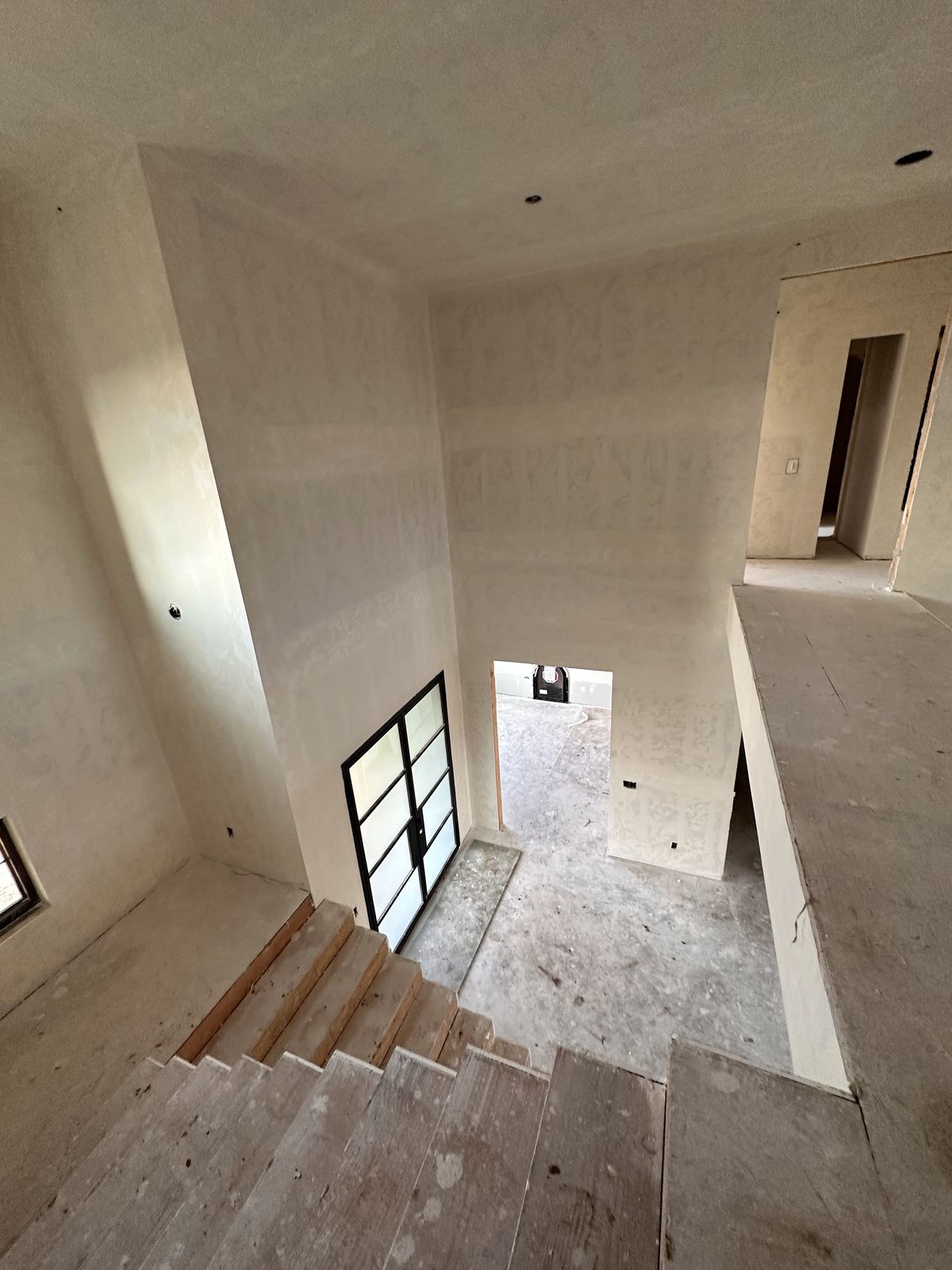 Interior of a house under construction, viewed from atop an unfinished wooden staircase